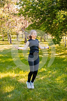 Young woman jumping rope on the lawn in a summer park. Jumping model. The concept of a healthy lifestyle and outdoor sports