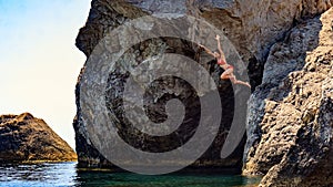 Young woman jumping to the sea from a cliff