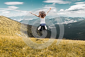 Young woman jumping on top of the summer mountains