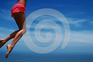 Young woman jumping on the tropical beach. Blue sky and slim legs