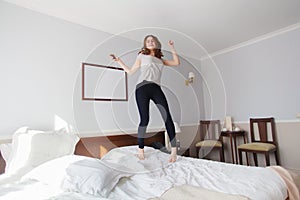 Young woman jumps on the bed in bright hotel room