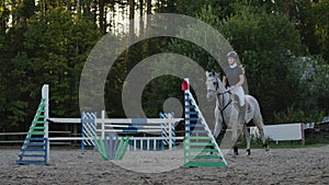 Young woman jumps horse over an obstacle during her training in an arena. Young woman jumps horse over an obstacle