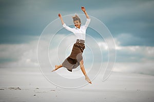 Young woman jumps on sand in desert and joyful laughs.