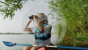 A young woman is kayaking on the river against a beautiful landscape and looking through binoculars. Travel. Tourism.