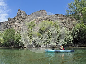 Young woman kayaks by rocky shore