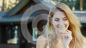 Young woman with keys from home. Smiling, looking at the camera. New wooden cottage in the background