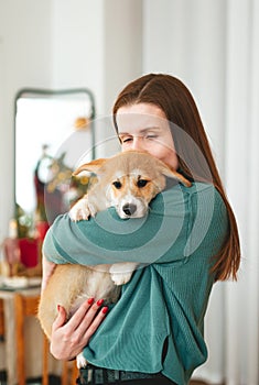 Young woman kissing her corgi puppy at home