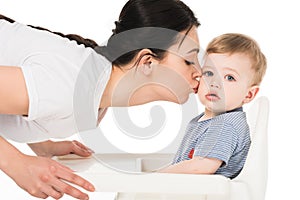 young woman kissing little son in highchair