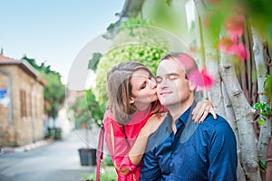 Young woman kissing a man on cheek. Fall in love romantic married couple in bright clothes on the street with blooming trees. Fami