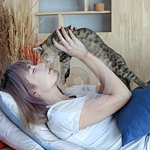 Young woman kissing a pussycat. A cat lying on a person. Asian young woman with cute cat lying in sofabed at home