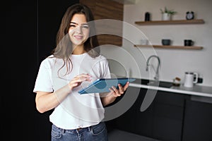 Young woman in kitchen during quarantine. Girl hold tablet in hands and working online. Remote home office