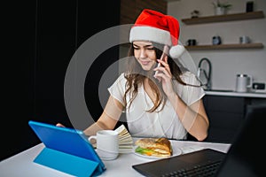 Young woman in kitchen during quarantine. Girl talking on phone and working using tablet. 2021 new year or christmas