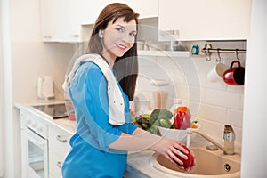 Young woman in the kitchen washing vegetables.