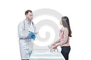 young woman with kitten on table and male veterinarian writing in clipboard