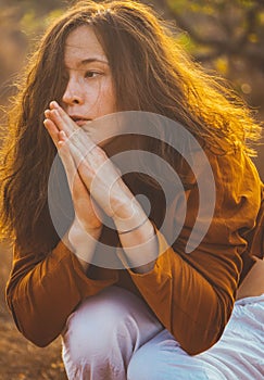 a young woman is kneeling on the ground with her hands clasped