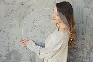 Young woman in knitted cardigan and warm socks wake up in the morning in cozy scandinavian bedroom and sitting on bed with white b