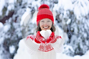 Young woman in knitted sweater holding heart shape snow ball in winter. Girl in family snow fight game. Female in knit handmade