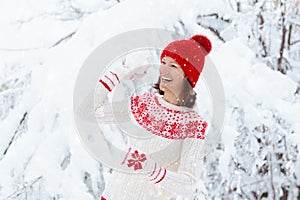 Young woman in knitted sweater playing snow ball fight in winter. Girl in family snow balls game. Female in knit handmade hat and