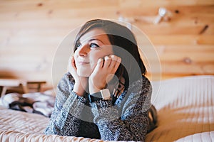 Young woman in a knitted sweater relaxing on a bed in a countryhouse