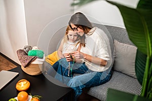 Young woman knitting with her daughter in cozy living room at home