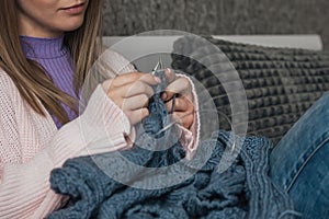 Young woman knitting warm sweater indoors.