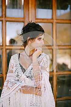 Young woman in a lace dress stands at the glass door with her head propped up. Portrait