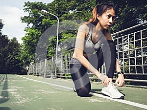 Young woman lace up her shoe ready to workout on exercising in the park with warm light sunshine in morning.