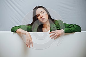 Young woman with lame face expression leaning on an edge of an empty bathtub