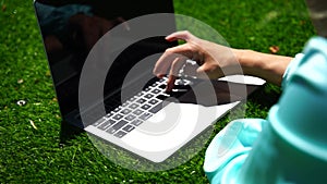 Young woman with laptop on the grass. Girl working on laptop in park