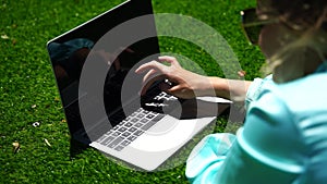 Young woman with laptop on the grass. Girl working on laptop in park