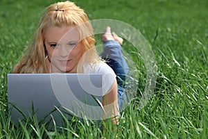 Young woman with laptop on green meadow