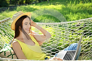 Young woman with laptop resting in comfortable hammock at garden