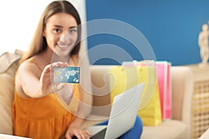 Young woman with laptop showing credit card at home. Online shopping