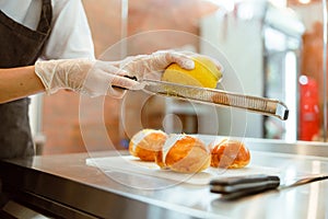 Woman grates fresh lemon zest above buns with cream at metal table photo