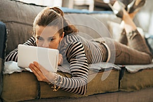 Young woman laying on couch and using tablet pc