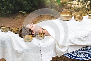 Young woman laying on a massage bed with tibetan singing bowl outdoor. Nepal copper singing bowl sound massage