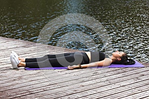 A young woman leading a healthy lifestyle and practicing yoga performs the shavasana exercise, lies on a mat in a park