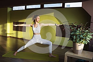 A young woman leading a healthy lifestyle and practicing yoga, performs the Virabhadrasana exercise, warrior pose