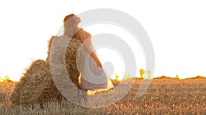 Young woman lean on haystack walking in summer evening, beautiful romantic girl outdoors in field at sunset
