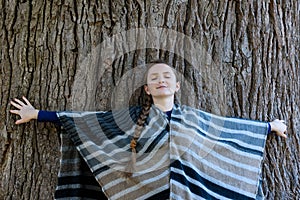 Young woman leaned her back against the trunk of a large tree. Closed eyes. Unity with nature