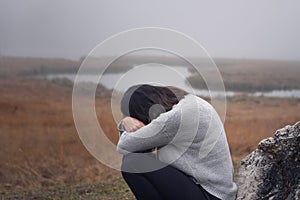 Young woman leaning against a stone with arms crossed in front of the face crying