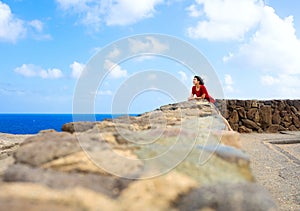 Young woman leaning against stone wall overlooking Hawaiian ocean