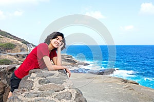 Young woman leaning against stone wall overlooking Hawaiian ocean