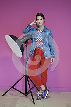 Young woman leaning against studio flashlight over a pink background