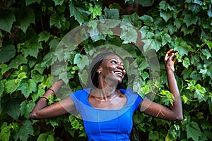 Young woman leaning against a wall covered with green leaves