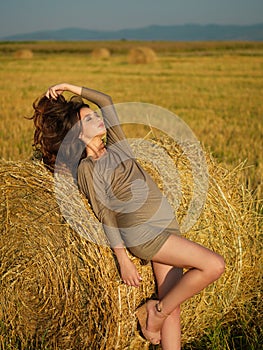 Young woman leaning hay stack enjoying breeze