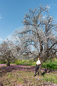 Young woman leaning and relaxing under almond blooming tree enjoying spring