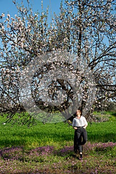 Young woman leaning and relaxing under almond blooming tree enjoying spring.