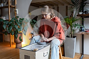 Young woman learning how to throw clay on pottery wheel while visiting ceramics masterclass.