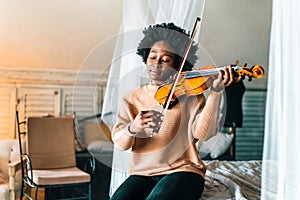 Young woman learning to play violin at home. Romantic african american girl playing violin